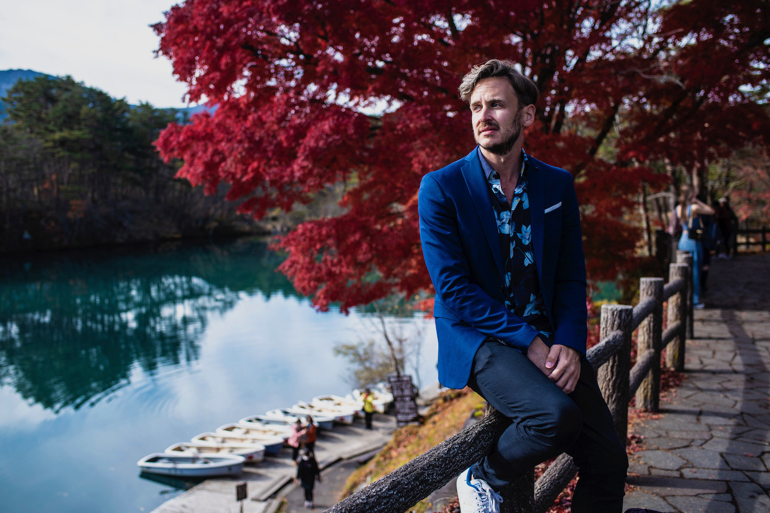 Man in a blue blazer in front of a red tree in Japan